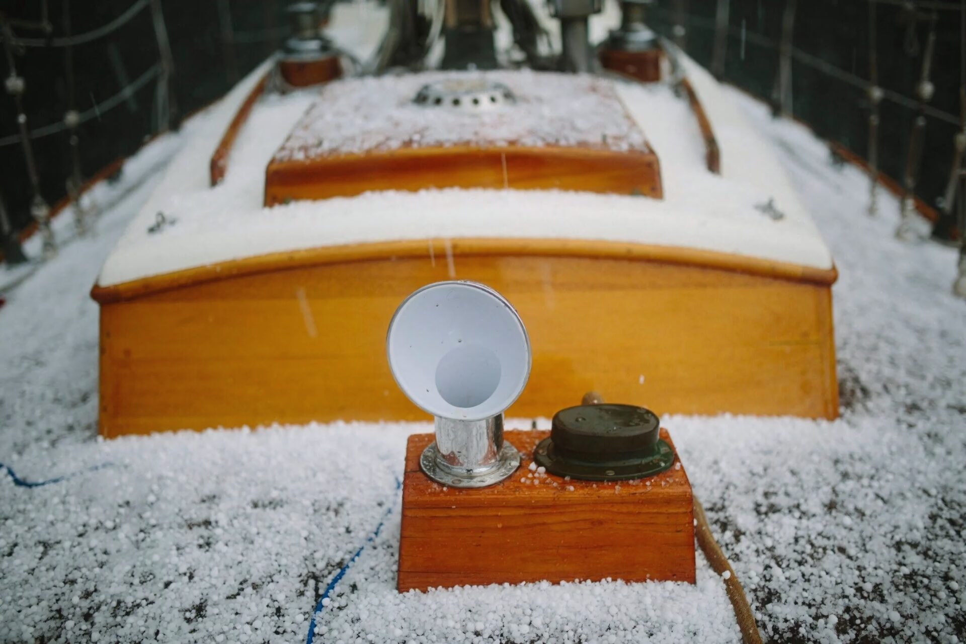 The varnished wooden foredeck of a sailboat, dusted with hailstones